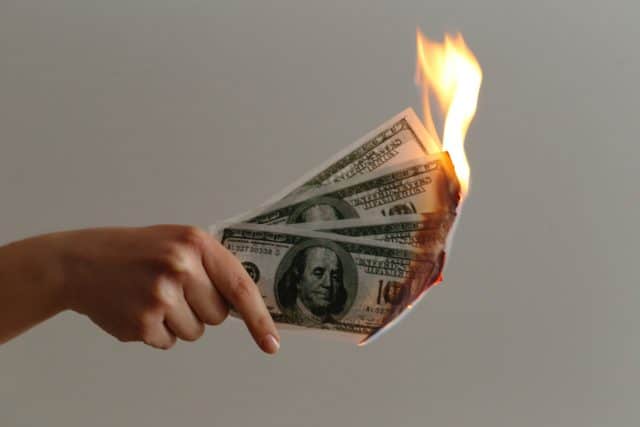 hand holding bank notes on fire |spend less than you earn |