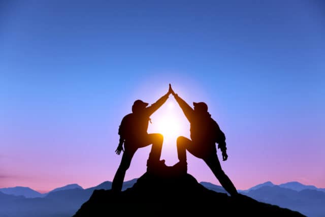 The Silhouette of two man with success gesture standing on the top of mountain