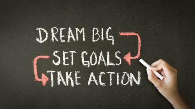 A person drawing and pointing at a Dream Big, Set Goals, Take Action chalk illustration