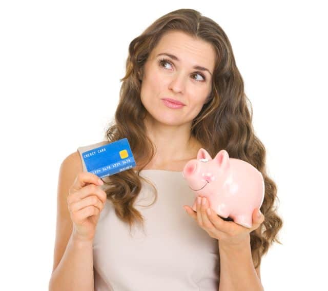 Thoughtful young woman holding credit card and piggy bank
